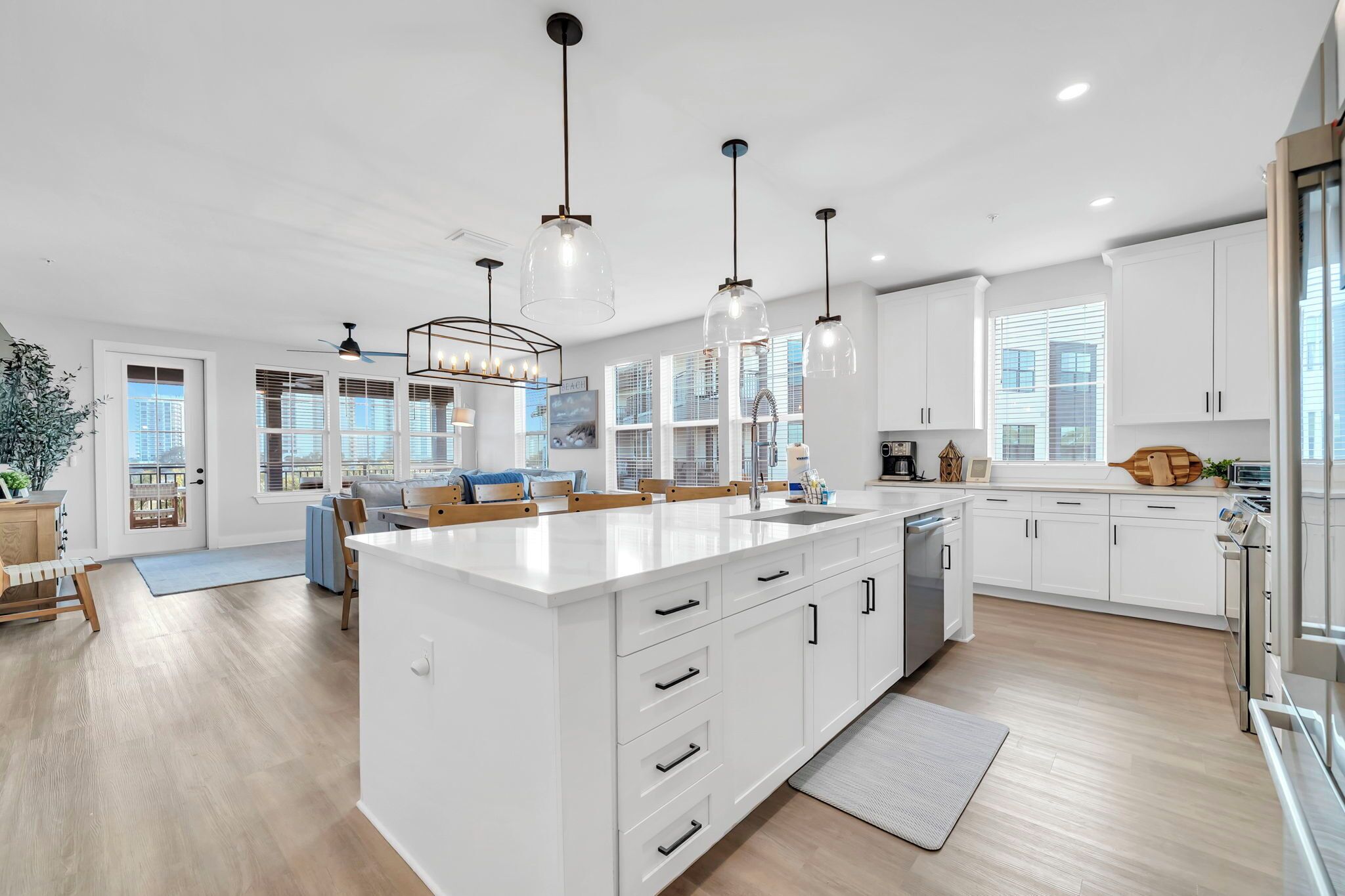 Una cocina moderna con armarios blancos, una isla grande con un lavamanos, luces colgantes y vistas a la ciudad a través de amplios ventanales.
