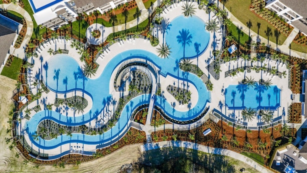 Vista aérea de un complejo turístico con una gran piscina central, piscinas más pequeñas y palmeras.
