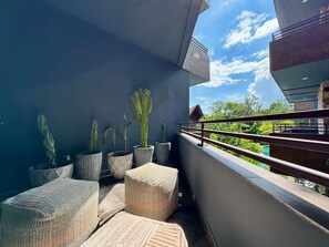 Ein Balkon mit Kakteen in Töpfen, Korbmöbeln und Blick auf Grün.