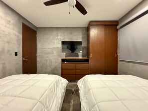Une chambre avec deux lits, un ventilateur de plafond, une armoire en bois et un petit miroir.