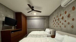 Une chambre avec deux lits, une télévision, un ventilateur de plafond et un mur agrémenté d’éléments décoratifs.