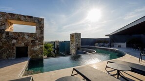 Une piscine à débordement située sur le toit, avec des murs en pierre et des chaises longues.