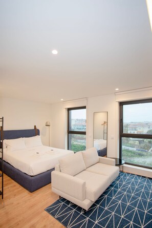 Ein modernes Hotelzimmer mit einem großen Bett, einer Couch, einem Spiegel und Blick auf die Stadt.