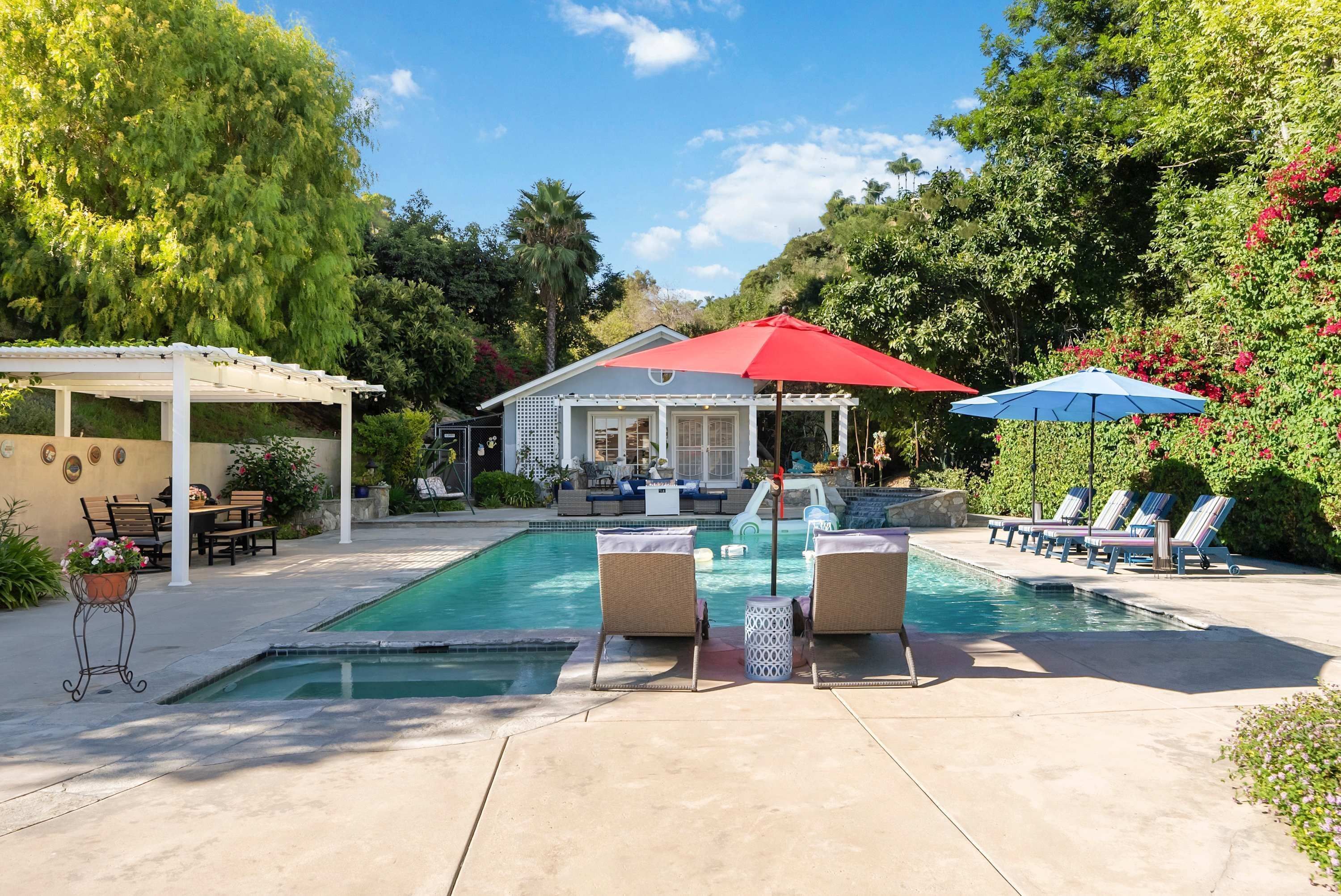 A backyard with a swimming pool, lounge chairs, and a covered patio area.