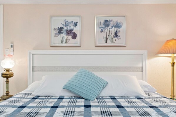 A neatly made bed with a checkered bedspread, a single blue pillow, and two framed floral paintings on the wall. - Luxury LA Garden Estate Private Pool Hottub Tennis (La Habra)