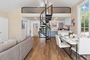 Un vaste espace de vie agrémenté d’un escalier moderne, d’une table à manger pour quatre personnes et d’un coin salon confortable.