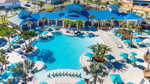 Uma piscina grande, com vários níveis, áreas de descanso ao redor e palmeiras.