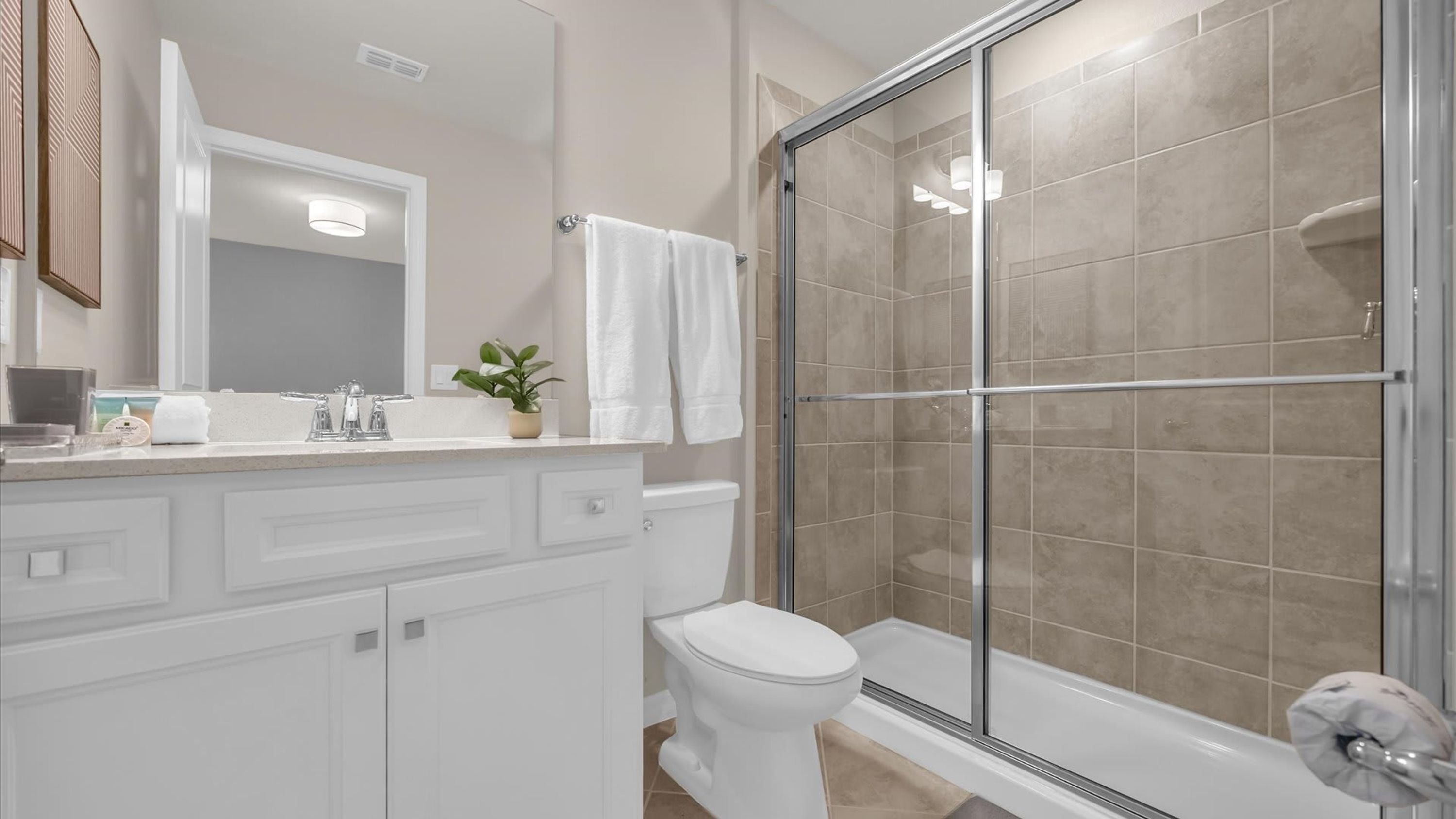 A modern bathroom with a glass-enclosed shower, a white toilet, and a vanity with a mirror and sink.