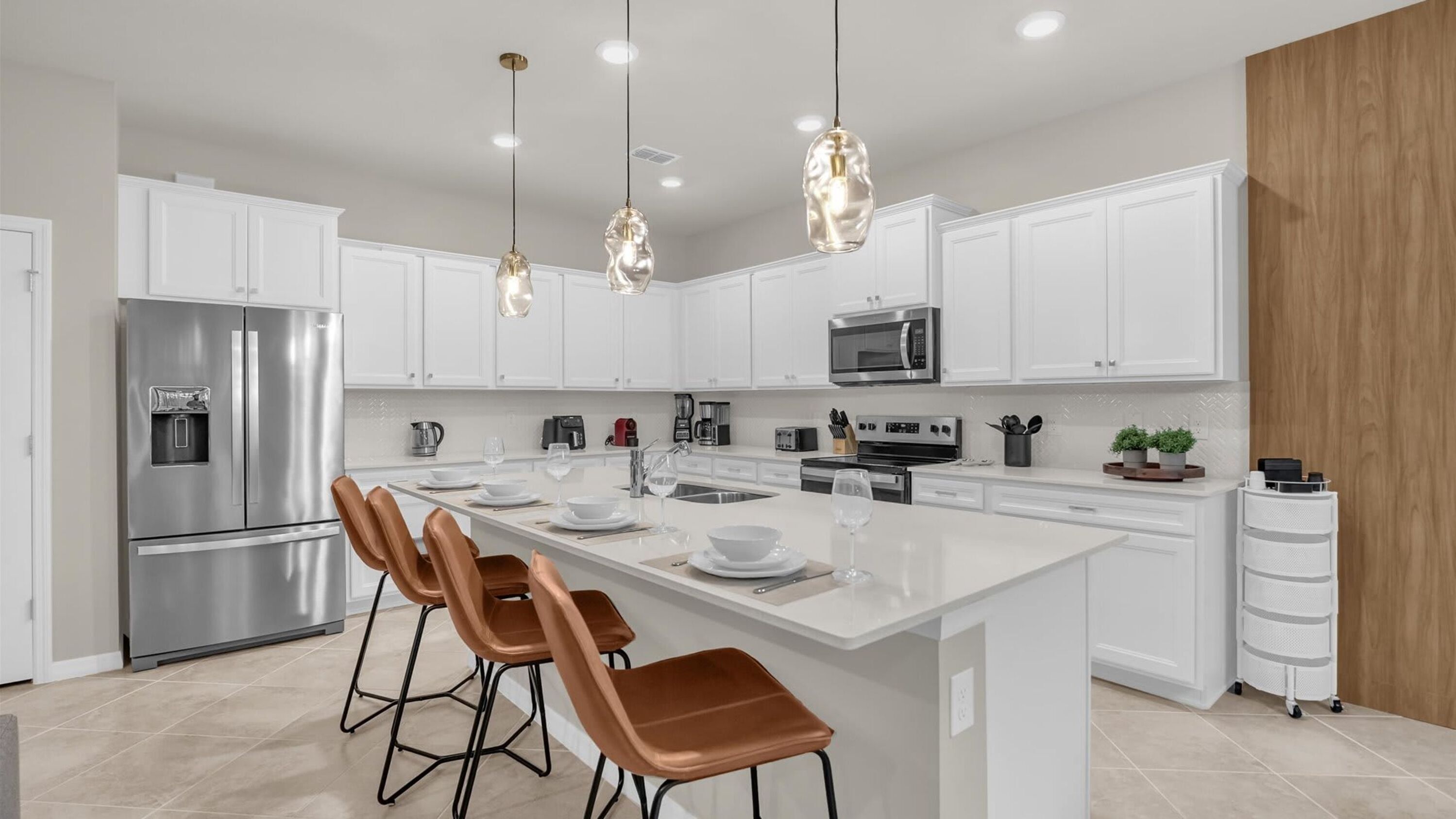 A modern kitchen with white cabinets, stainless steel appliances, a central island with bar stools, and pendant lighting.