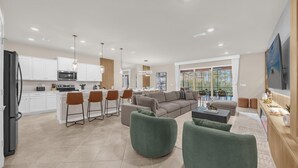 A modern kitchen with white cabinets, a black refrigerator, and a dining area with a large window. - Stunning Resort Villa w Pool Cinema Games Room (Clermont)