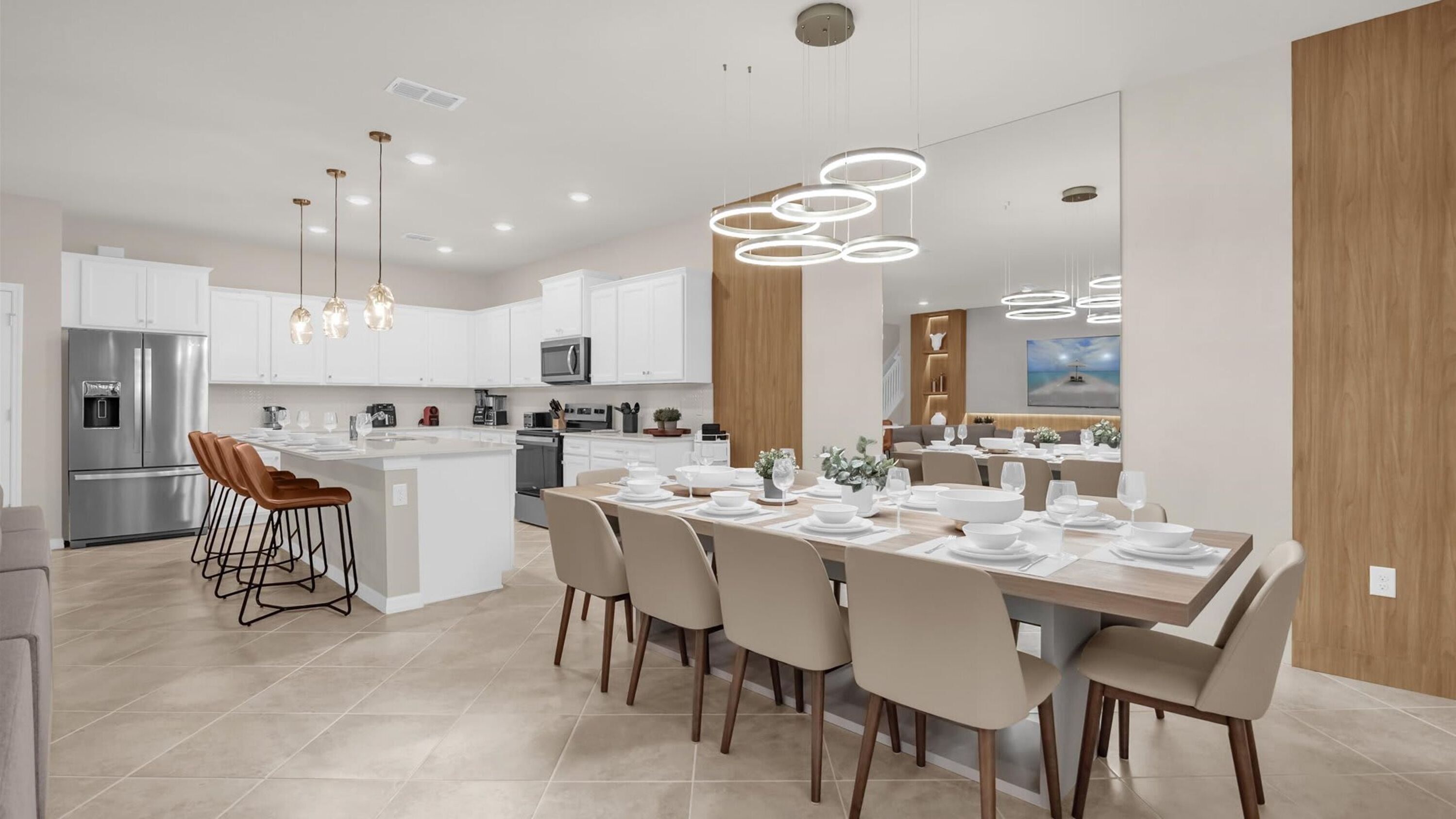 A modern kitchen with white cabinets, a stainless steel refrigerator, and a dining area with a large island and multiple chairs.