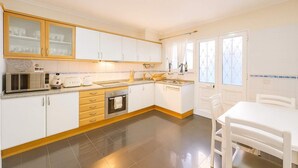 Cocina moderna con armarios blancos, microondas, tostadora y fregadero. Hay una mesa de comedor con sillas.