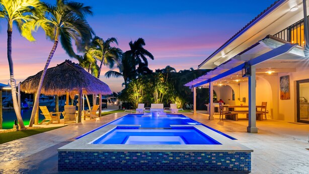 A swimming pool with lounge chairs, a thatched-roof hut, and a covered patio area. - Deep Blue Waterfront Gem Pool Kayaks Dock (Key Colony Beach)