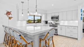 A modern kitchen with white cabinetry, a large island with bar stools, and pendant lighting. - Deep Blue Waterfront Gem Pool Kayaks Dock (Key Colony Beach)