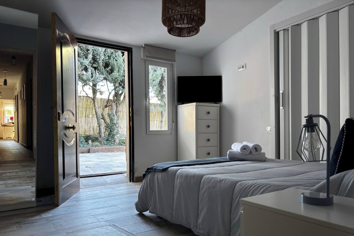 A bedroom with a bed, a dresser, a TV, and a view of the outdoors.