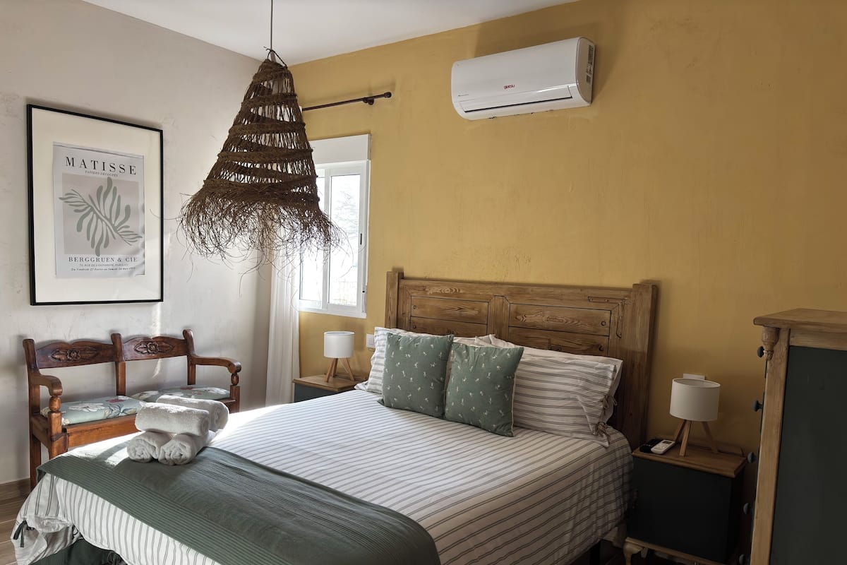 A neatly arranged bedroom with a bed, bedside tables, a hanging light fixture, and an air conditioning unit.