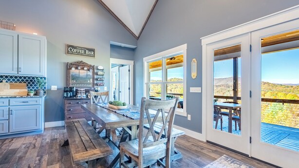 A kitchen with a long wooden table, a coffee bar sign, and a view of the outdoors through large windows. - MTN Retreat, 5 Bdrm, Pool, Hot Tub, Game Rm, Theater, Putt-Putt, Fireplace. (Dahlonega)