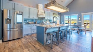 A modern kitchen with a central island, bar stools, and a view of the outdoors. - MTN Retreat, 5 Bdrm, Pool, Hot Tub, Game Rm, Theater, Putt-Putt, Fireplace. (Dahlonega)
