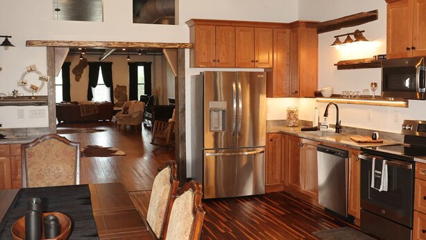 A modern kitchen with wooden flooring, stainless steel appliances, and a dining area with a long table and chairs. - Historic meets modern renovation is this downtown gem. (Buffalo)
