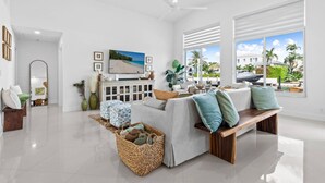 A spacious living room with a large window, a ceiling fan, and a view of the beach. - Waterfront Oasis Heated Pool Game Room Gym (Deerfield Beach)