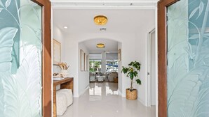 A hallway with a white floor, a wooden bench, a potted plant, and a framed picture on the wall. - Waterfront Oasis Heated Pool Game Room Gym (Deerfield Beach)