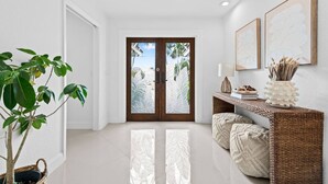 A modern interior with a wooden door, a potted plant, a console table with decorative items, and a ceiling light fixture. - Waterfront Oasis Heated Pool Game Room Gym (Deerfield Beach)