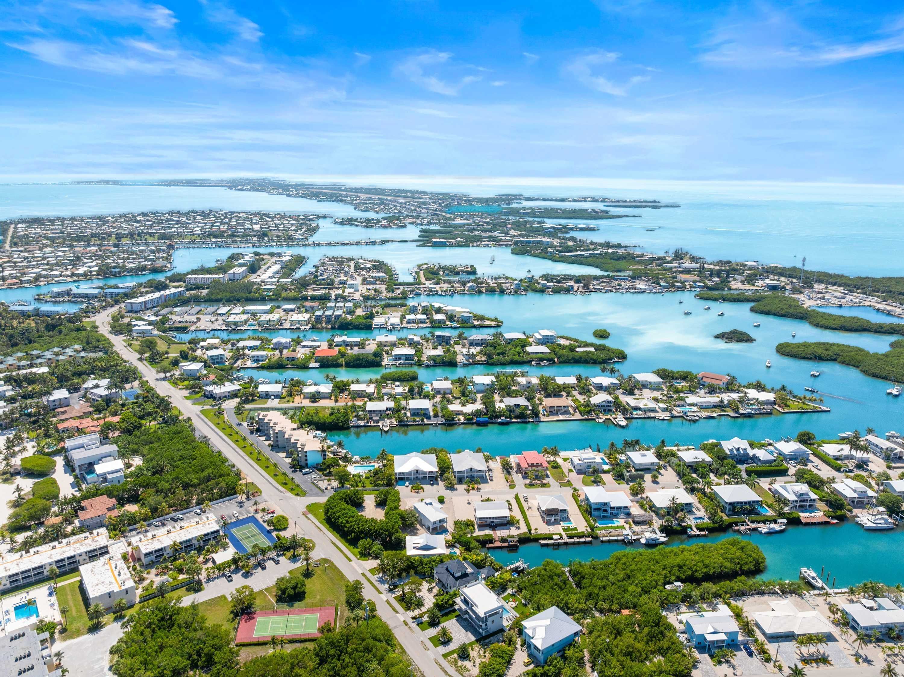 An aerial view of a coastal residential area with multiple small houses, a marina, and clear blue waters.