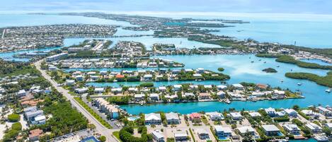 An aerial view of a coastal residential area with multiple small houses, a marina, and clear blue waters.