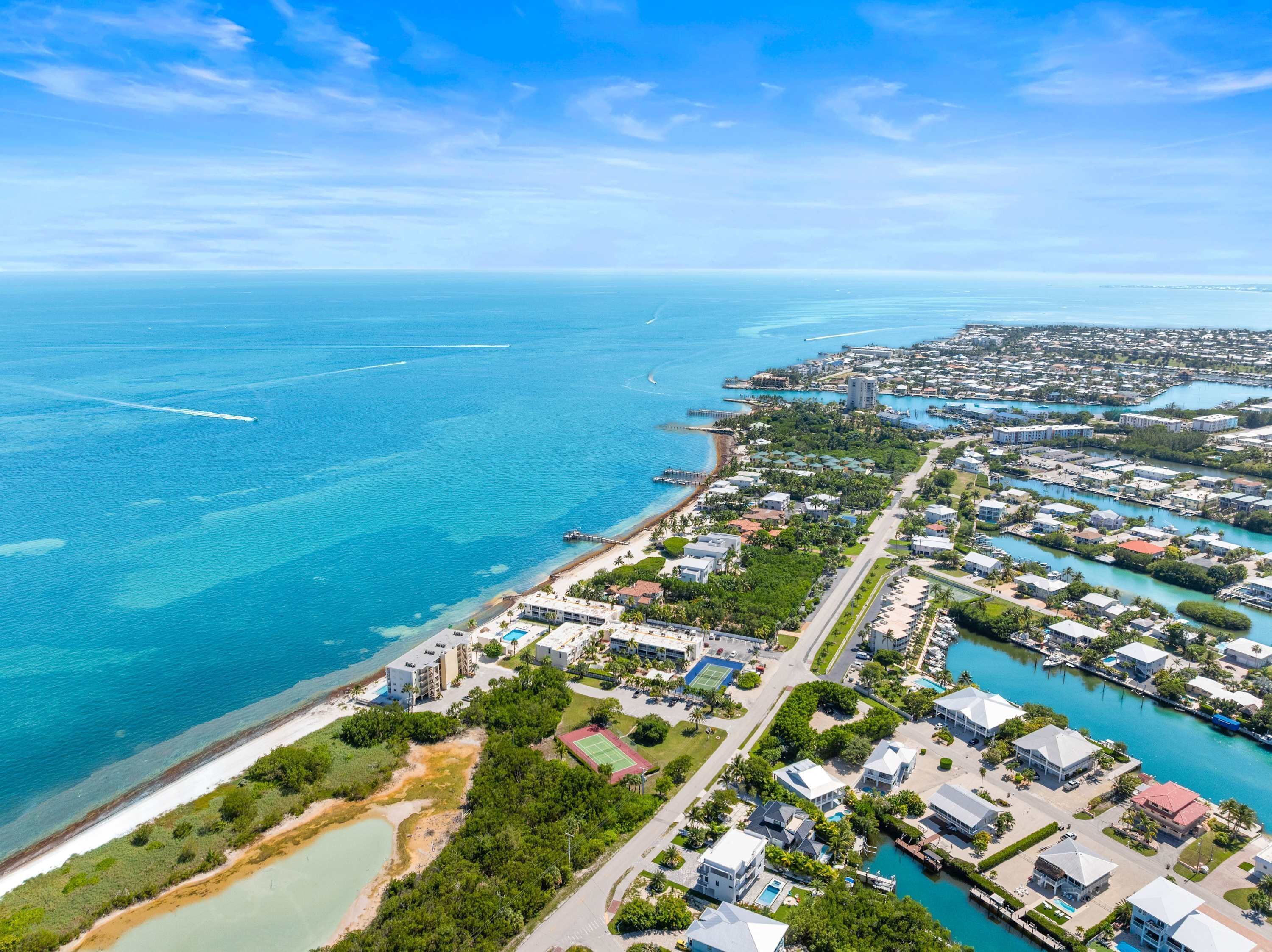 An aerial view of a coastal residential area with houses, a beach, and a marina.