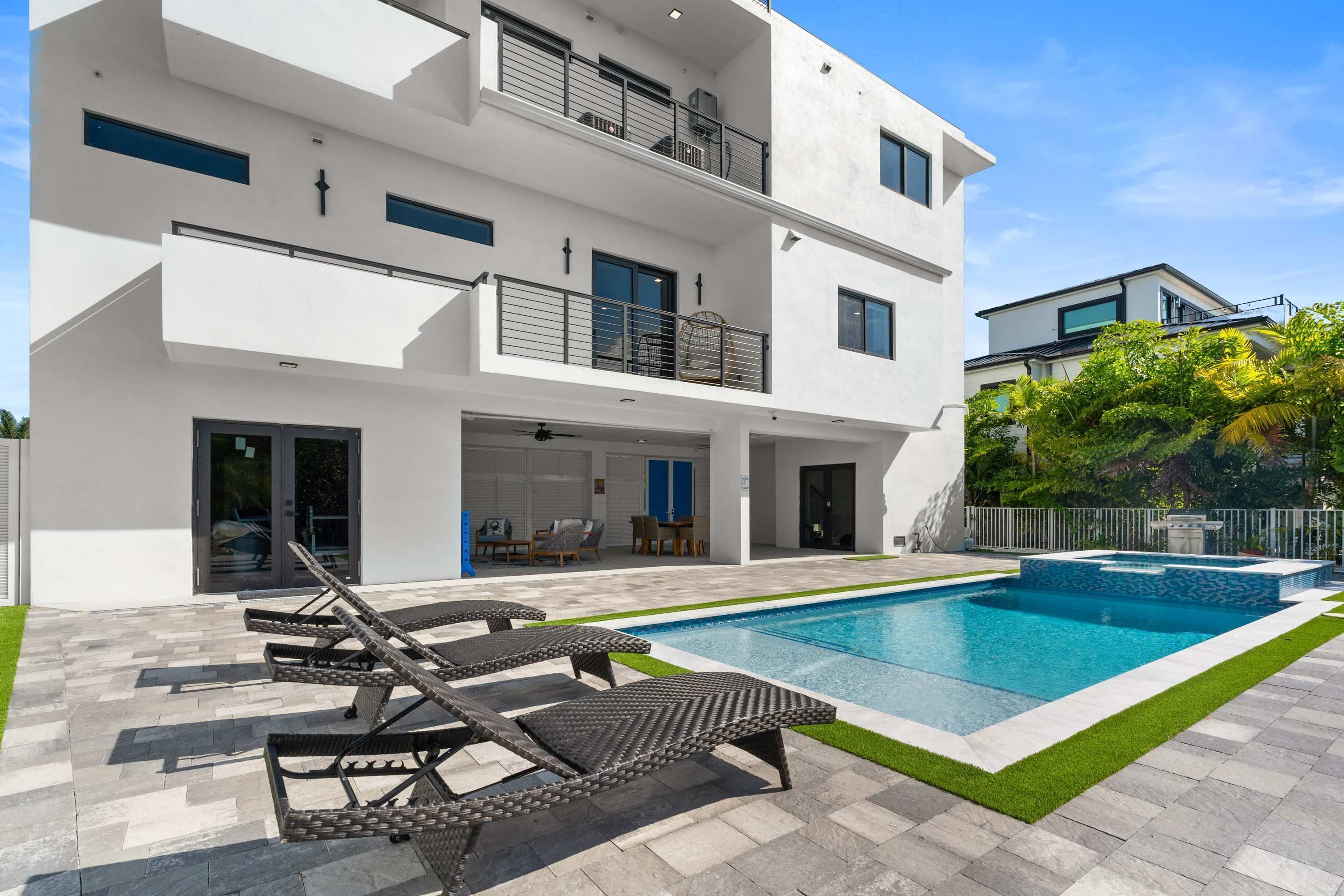 Una casa moderna de dos pisos con piscina, mobiliario exterior y césped cuidado.