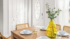Una mesa de comedor con platos blancos, vasos y un jarrón amarillo con follaje.