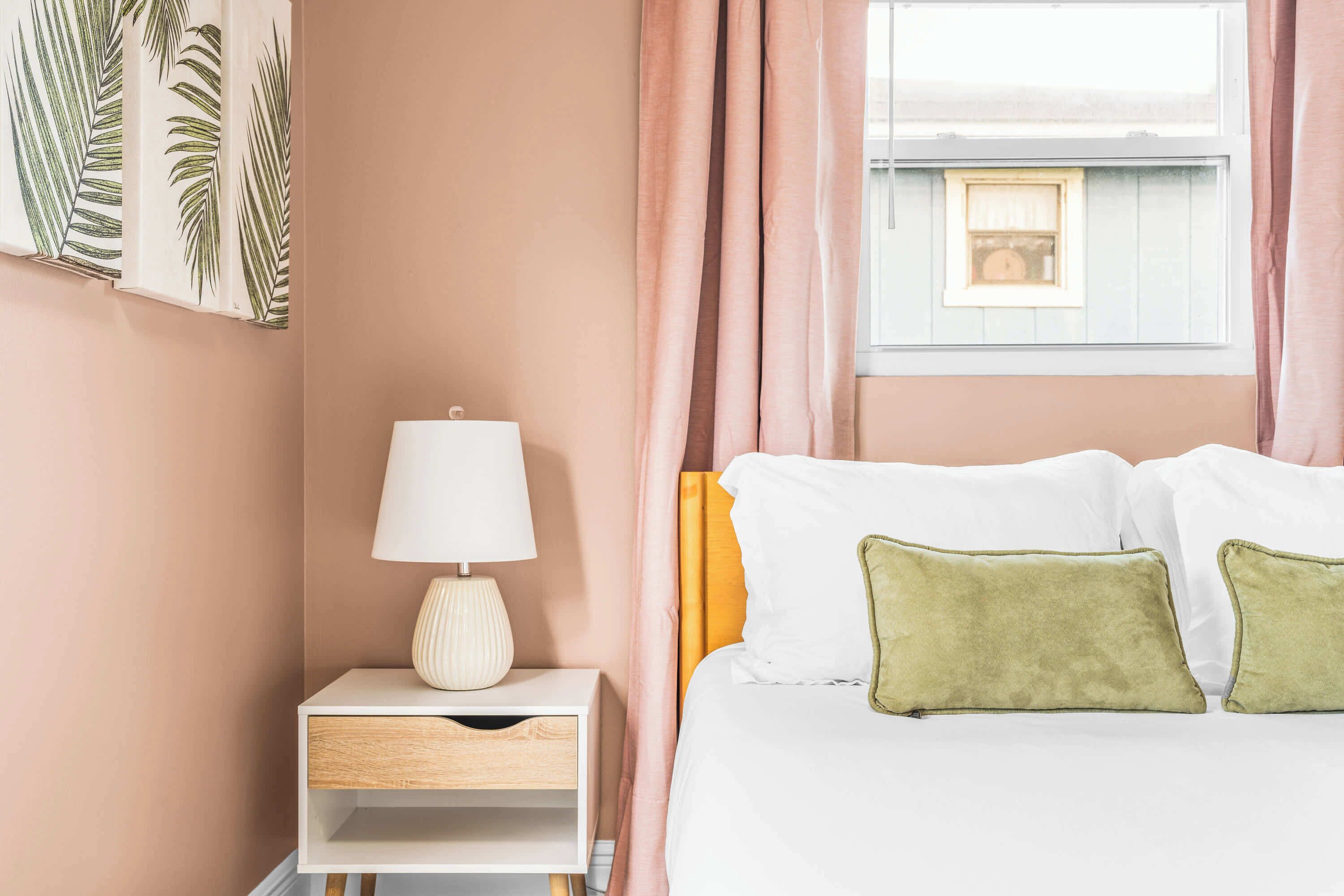 Ein Schlafzimmer mit einem Bett, einem Nachttisch mit Lampe und einem Fenster mit Vorhängen.