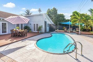 A swimming pool with a wooden deck and a covered patio area. - Heated Pool Days & Palm Nights – Modern West Palm Vibes (West Palm Beach)