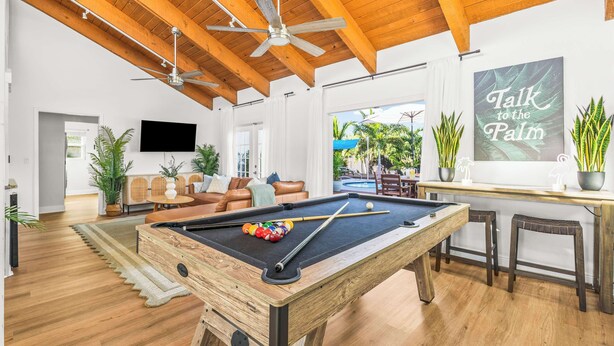 Una mesa de billar en una sala amplia con vigas de madera, un espacio de descanso acogedor y vistas al exterior.