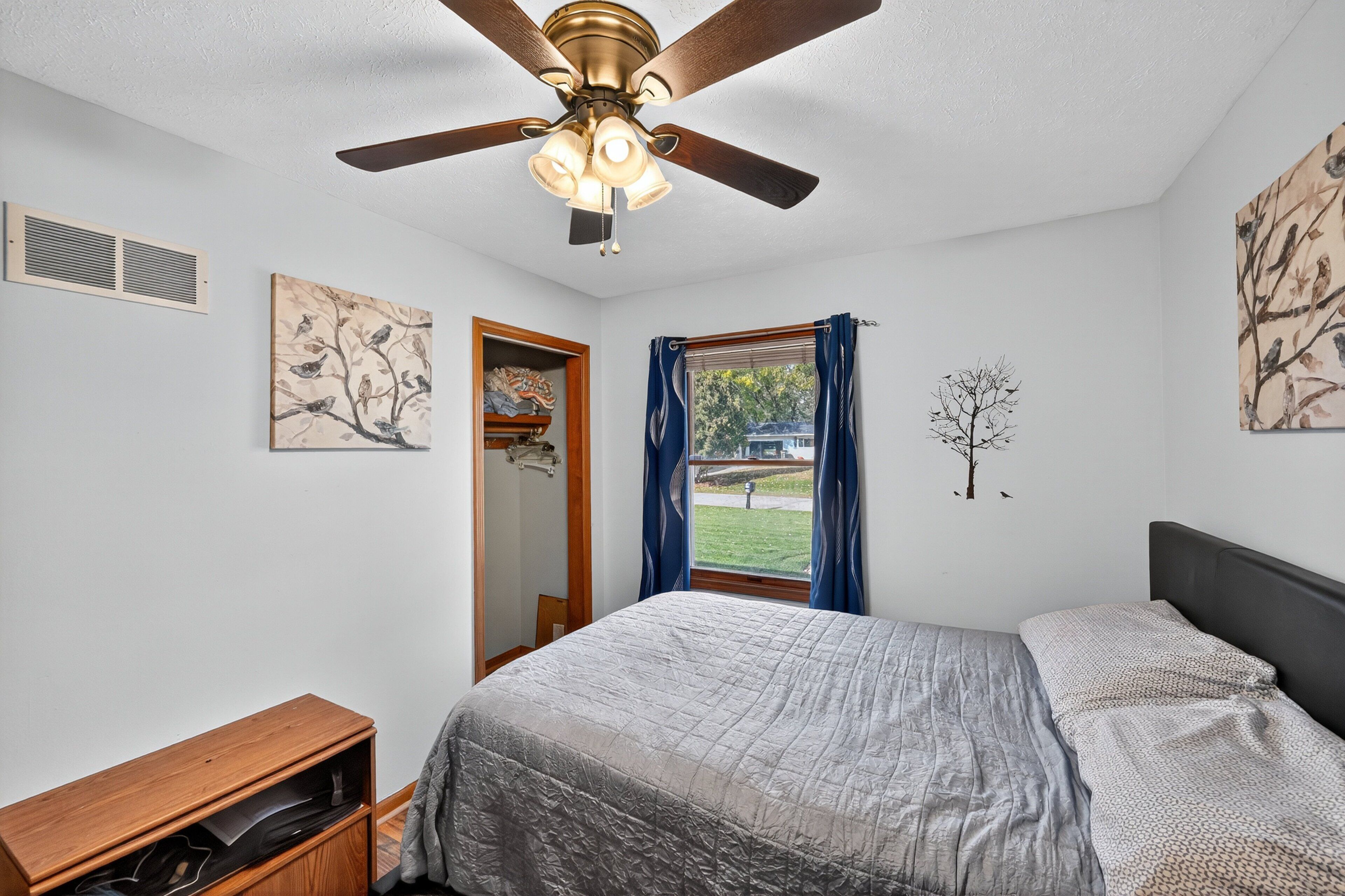 A bedroom with a bed, a ceiling fan, a window with curtains, and wall art.