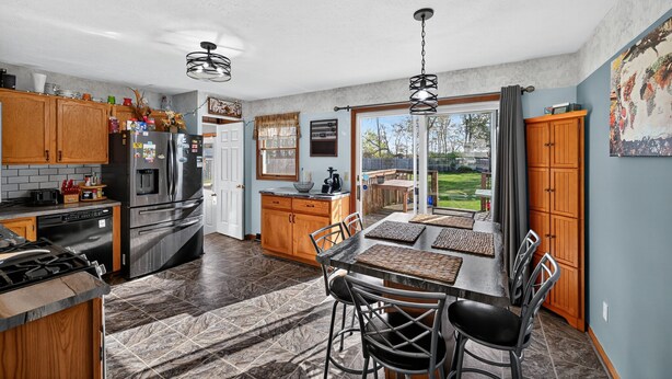 A modern kitchen with wooden cabinets, a stainless steel refrigerator, and a dining area with a table and chairs. - Cozy Retreat With Hot Tub In Peaceful Goshen 4 Bedroom Home (Goshen)