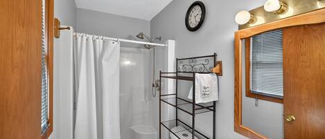 Een badkamer met een douche, toilet, wastafel, handdoekrek en een klok aan de muur.