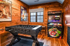 A room with a foosball table, posters, a window, and a retro arcade machine. - Pearl's Mountain Retreat 3 Bedroom Cabin (Sevierville)