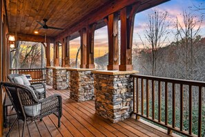Eine überdachte Veranda mit Steinpfeilern, Korbstühlen und Blick auf Bäume und Hügel.