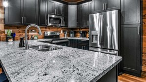 Une cuisine moderne avec des meubles de couleur sombre, des appareils électroménagers en acier inoxydable et un plan de travail en granit.