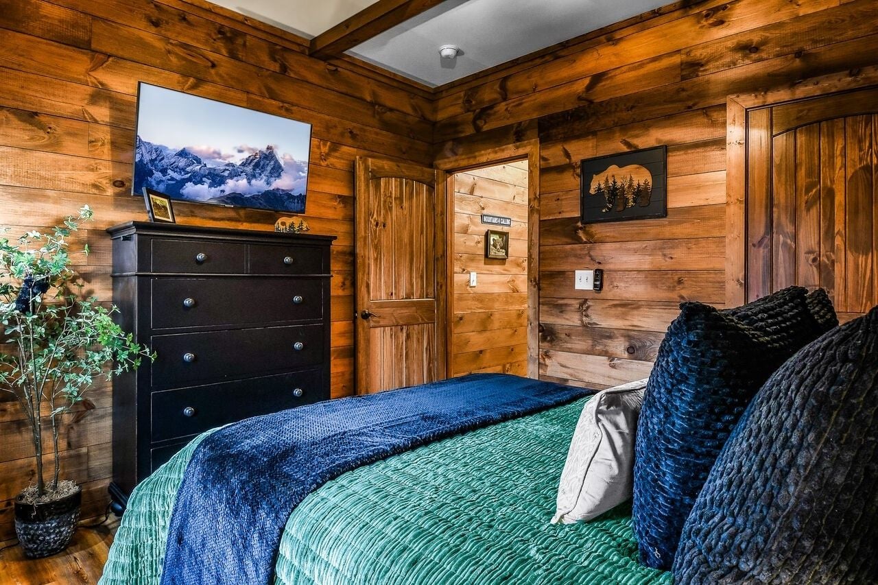 Ein Zimmer mit Holzwand, einem Bett, einem Schminktisch und einem Fernseher an der Wand.
