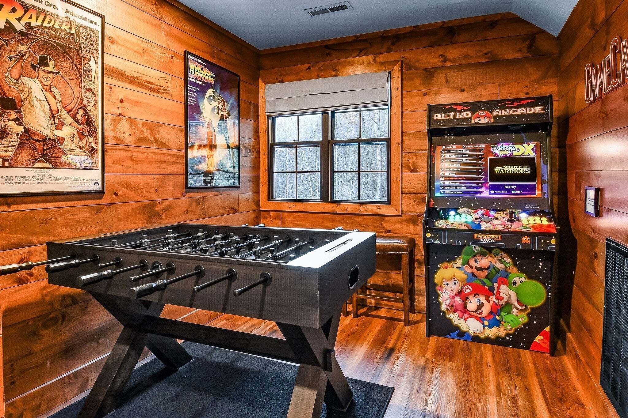 A room with a foosball table, posters on the wall, a window, and a retro arcade machine.