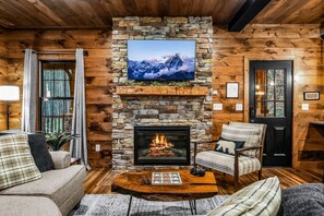 A cozy cabin interior with a stone fireplace, a mounted TV, and wooden walls. - Pearl's Mountain Retreat 3 Bedroom Cabin (Sevierville)