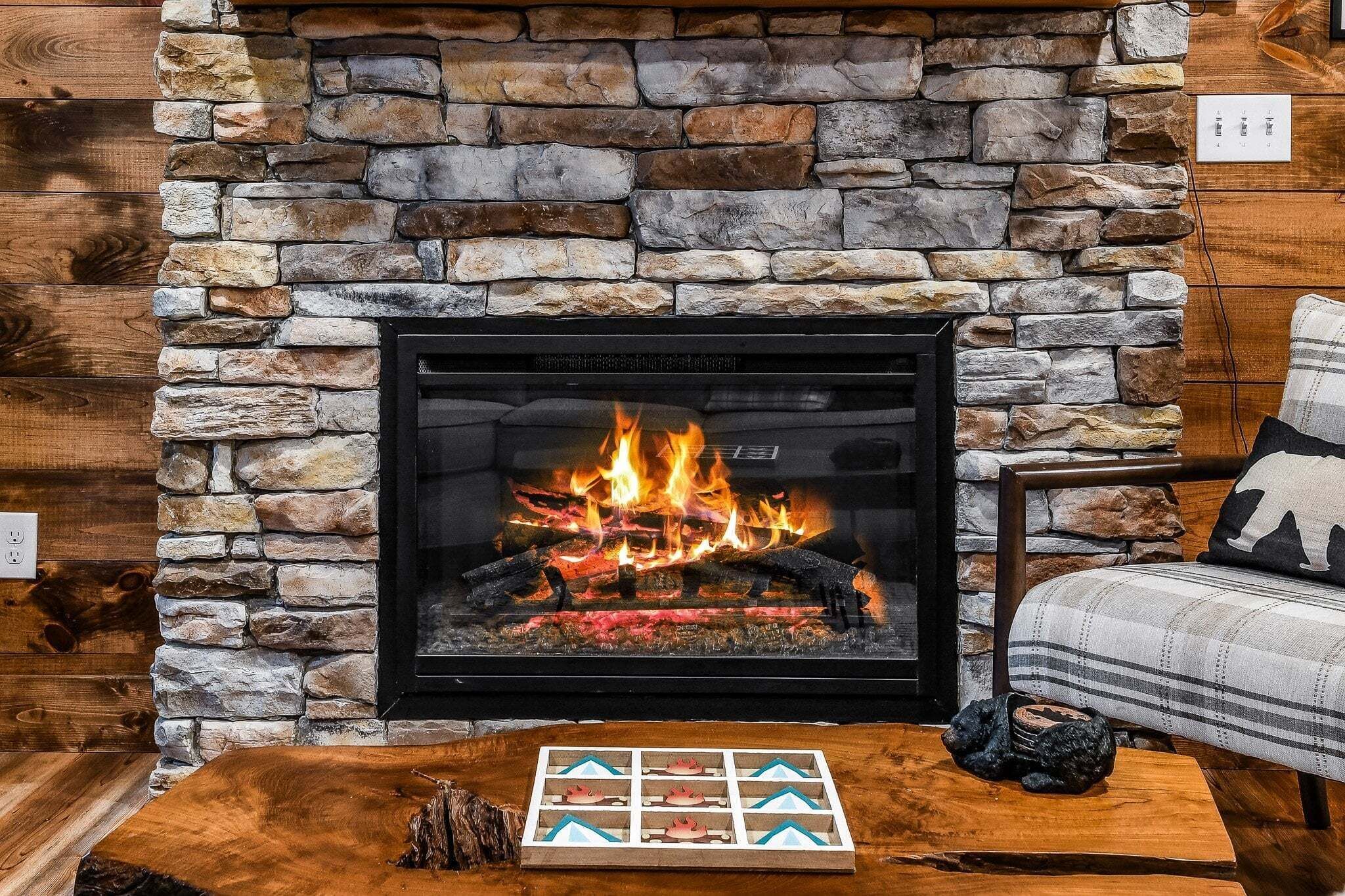 A stone fireplace with a fire, a wooden coffee table, and a plaid sofa.