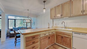 A modern kitchen with wooden cabinets, a large island with a sink, and pendant lighting. - Slopeside Condo with Tree View (Mammoth Lakes)