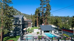 A modern building with a swimming pool, surrounded by tall trees and a mountainous backdrop. - Slopeside Condo with Tree View (Mammoth Lakes)