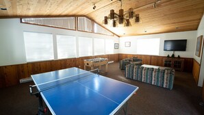 A room with a ping pong table, a foosball table, a sofa, and a television. - Slopeside Condo with Tree View (Mammoth Lakes)