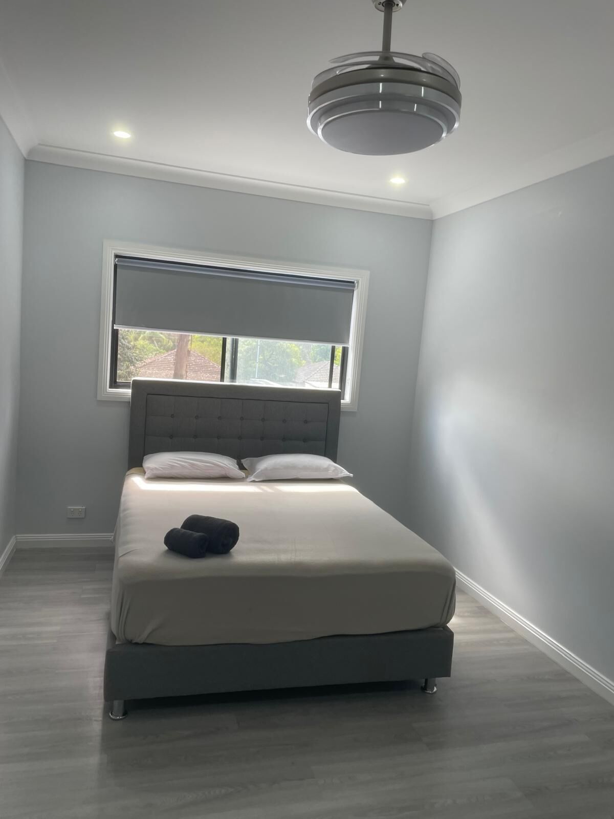A bedroom with a bed, a window with blinds, a ceiling light, and a view of the outside.