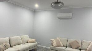 Een moderne woonkamer met twee lichte banken, een houten vloer, een plafondlamp en een airconditioner.