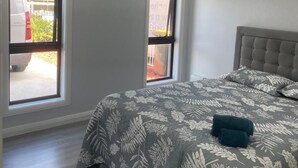 Een slaapkamer met een groot bed, twee ramen en een plafondventilator.